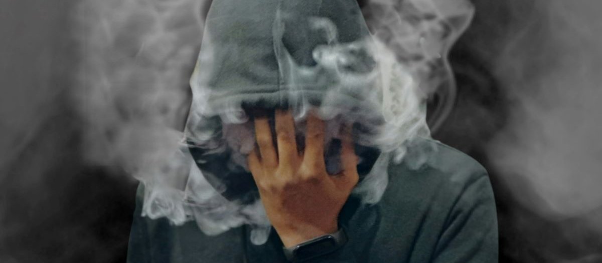 A man in a hoodie covers his face with smoke