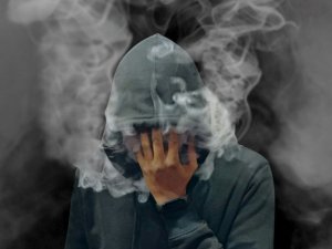 A man in a hoodie covers his face with smoke