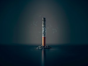 A single cigarette stands on end, with a black background 